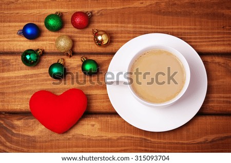 Cup of coffee, heart and christmas bubbles on wooden background.

