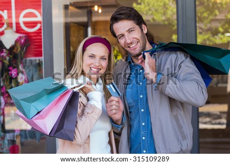 Portrait of smiling couple with shopping bags in front of window at shopping mall