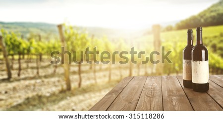 sunny landscape of vineyard with green leaves and bottles of wine on table 