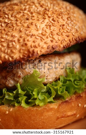One big delicious appetizing fresh burger of green lettuce leaf cheese meat cutlet and white bread bun with sesame seeds closeup, vertical picture