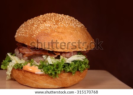 One appetizing big delicious fresh burger with green lettuce red tomato cheese cabbage bacon slice meat cutlet and white bread bun with sesame seeds on black background copyspace, horizontal picture
