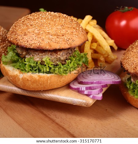 Big tasty appetizing fresh burger of green lettuce red tomato cheese and bacon slice meat cutlet and white bread bun with sesame seeds chips and violet onion closeup, square picture