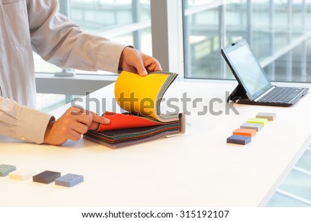 hands looking through color fabric swatches on desk with colored tiles
