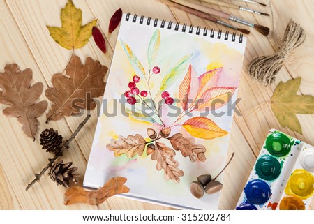 Notepad with watercolor paintings autumn leaves. View of workplace artist 