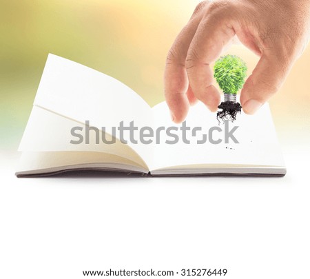 Earth day concept: Human hand adding light bulb of tree into the book over blurred sunset background