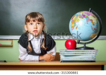 school, girl, schoolgirl 6 years in a black dress and a white shirt with two pigtails on the table Globe and red apple, microscope