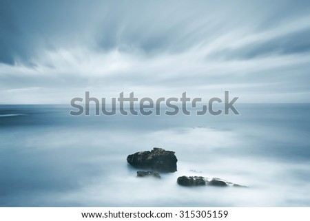 Dark rocks in a blue ocean under cloudy sky in a bad weather. Long exposure photography