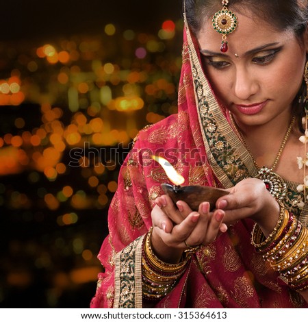Indian female in traditional sari lighting oil lamp and celebrating Diwali or deepavali, fesitval of lights at temple. Woman hands holding oil lamp, beautiful lights bokeh background.
