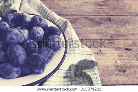 Plate full of fresh plums on a wooden background. Photo with colorful toned vintage filter effect.