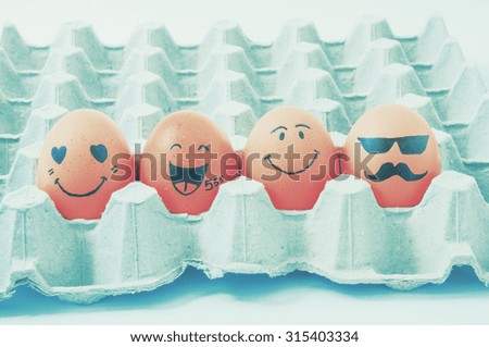 four brown eggs  with faces drawn  arranged in carton