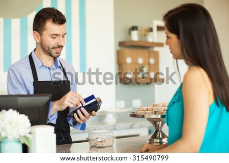 Male employee in a cake shop swiping a credit card in a bank terminal at the cash register in front of a customer