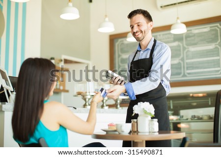 Young Hispanic waiter taking a credit card from a customer in a coffee shop