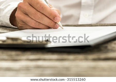 Closeup low angle view of male hand signing subscription form, legal document or business contract. Focus to the tip of the pen.