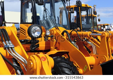 Bulldozer headlight, row of huge orange powerful construction machines, tractors, excavators, focused on spotlight, blue sky and white clouds on background, selective focus  Royalty-Free Stock Photo #315543863