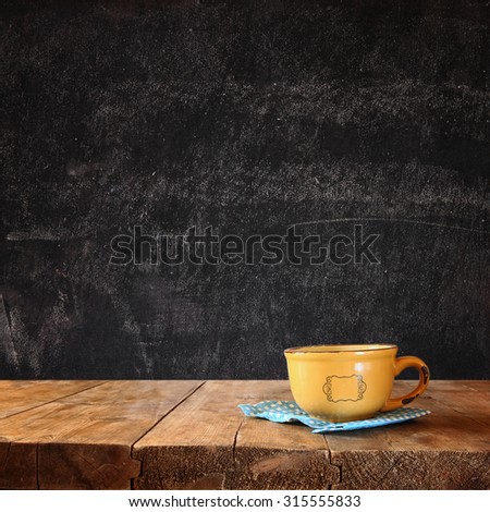 front image of coffee cup over wooden table and autumn leaves in front and blackboard background with room for text
