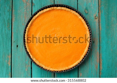 Fresh round bright orange homemade pumpkin pie in baking dish on turquoise table