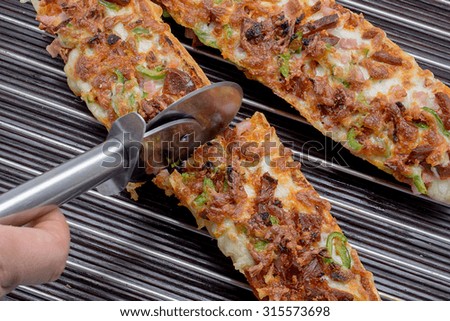 Cutting pizza baguette with mozzarella, green pepper, onion, tomato, bacon and sausage