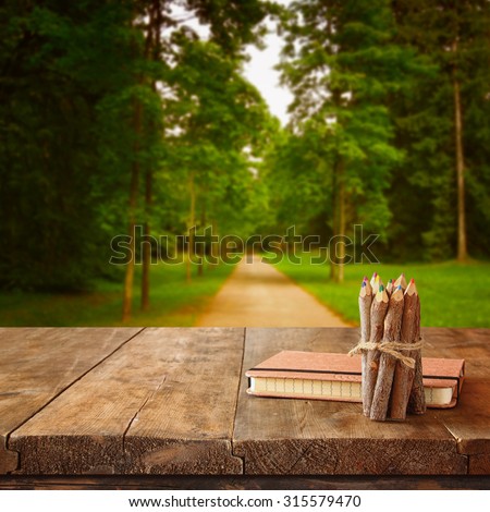 vintage notebook and stack of wooden colorful pencils on wooden texture table in front of countryside forest view