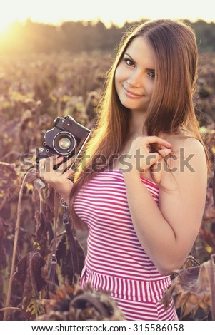 Beautiful young girl on the dry sunflower meadow take some pictures with his retro camera. Color effects and custom white balance added to this picture