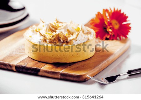 Lemon meringue pie on a timber board with a flower and plate in the background 