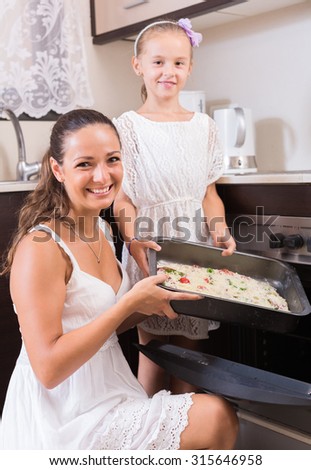 Happy housewife with little girl cooking Italian pizza in electric oven