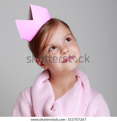 Studio image of a beautiful cheerful little girl in a pink knitted dress with a crown on his head on a gray background on Holiday