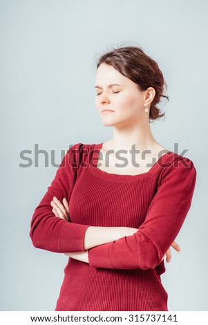 Young woman with the sour look crossed her arms. On a gray background.