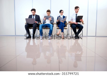 Photo of young creative business team of four with documents and computers. They sitting in a row and working. One man wearing informal clothes