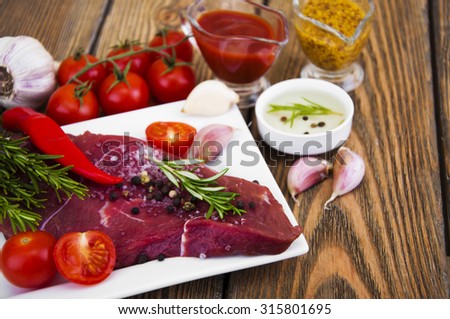 Fresh beef steak on plate with aromatic spices and sauce on a wooden background