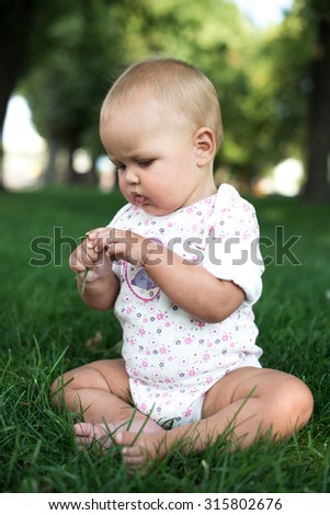 Happy baby with light and fluffy hair sitting on the grass and laughing. Summer and very warm. Happy smile.