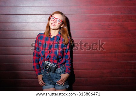 Pretty photographer. Attractive young woman with camera standing against wall.