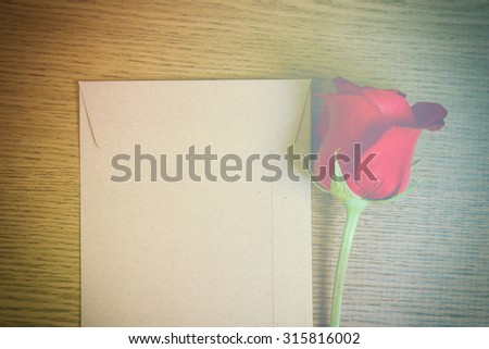 Beautiful red rose and brown envelope on a wooden floor. Vintage tone