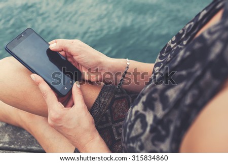 Cropped shot view of female person using cell telephone with copy space area on the screen while enjoying her recreation time, woman reading text message on her mobile phone while resting outdoors