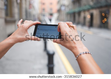 Cropped shot view of woman's hand photographing street view on mobile phone camera for social network picture, female taking picture on her smart phone for mobile chatting while walking on the street