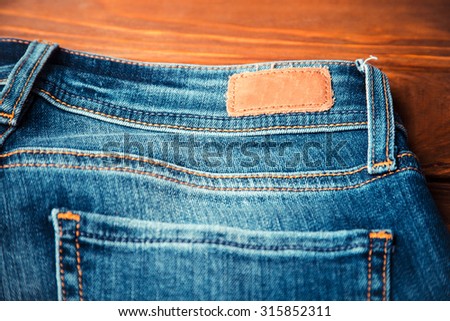 blue jeans with half of back pocket and brown leather tag on wood table background. Shallow depth of field. 