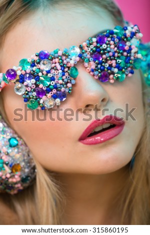 Studio photo of blonde girl in the style of art. Girl music fan in the headphones and glasses with rhinestones