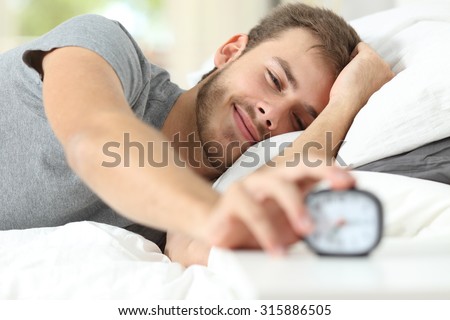 Happy wake up of a happy man lying on the bed and stopping alarm clock Royalty-Free Stock Photo #315886505