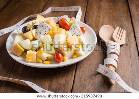 fresh healthy fruit salad and measuring tape on wooden background, Diet concept.