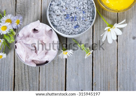 yellow calendula cream in glass pot, moisturizer and bath salt with white herbal flowers on weathered rusty wooden table background