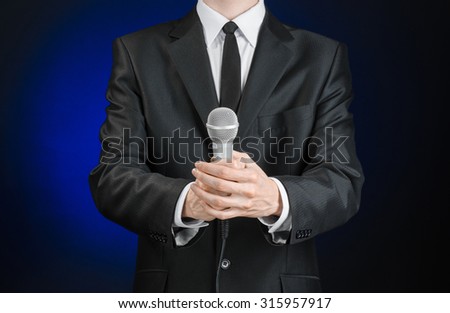 Business and speech topic: a man in a black suit holding a microphone on a gray dark blue isolated background in studio