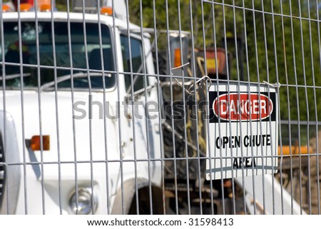 A construction truck shot behind steel fencing, with a danger sign affixed.
