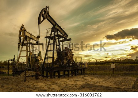 Oil pump jacks at sunset sky background. Toned.