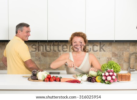 Middle-aged woman cutting vegetables in the kitchen. Her husband helping her. Happy couple cooking lunch or dinner for the whole family.