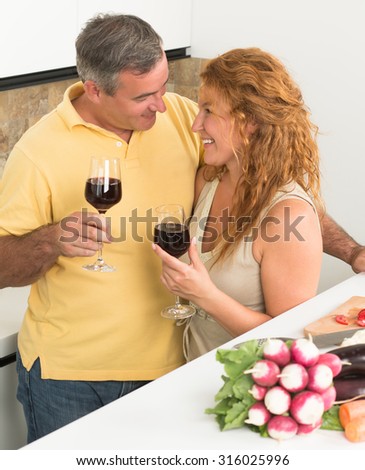 Cheerful mature couple spending their day at home. Man and woman smiling and holding glasses with delicious red wine.