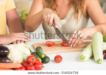 Close-up picture of woman cutting tomatoes in the kitchen. Man and woman preparing vegetables salad for lunch or dinner.