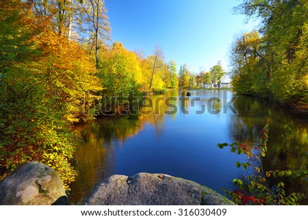 Colorful autumn trees near the river in park. Blue sky reflected in calm water. Landscape in sunny day