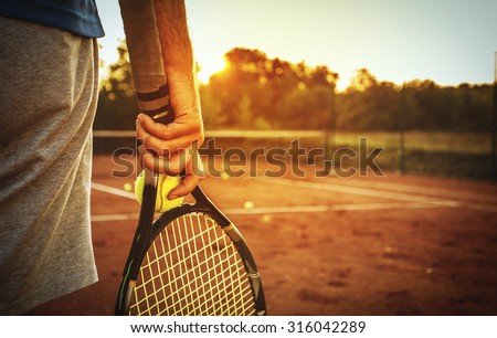Close up of man holding tennis racket on clay court. In his hand is tennis ball. On court is sunset./Man holding tennis racket Royalty-Free Stock Photo #316042289