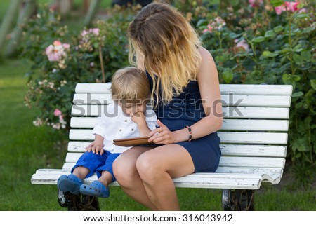 Little boy sitting with his mother on bench and looking to iPad.