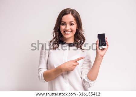 Smiling woman is pointing on smartphone standing on white background.
