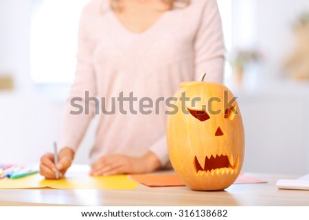 Lets make party. Craved pumpkin standing on the table with nice upbeat woman painting on the background
